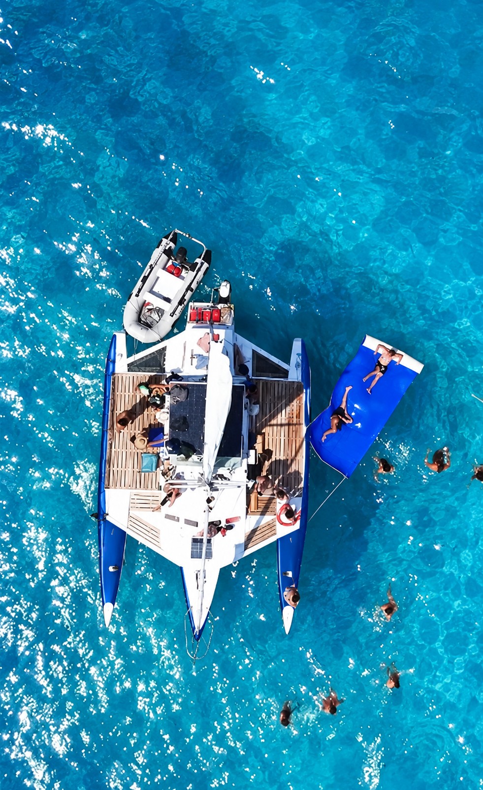 An aerial view of our three-hulled trimaran, wooden decks and guests swimming alongside